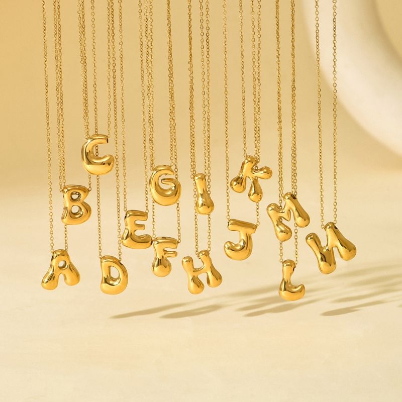 Gold necklaces with letter pendants on a beige background